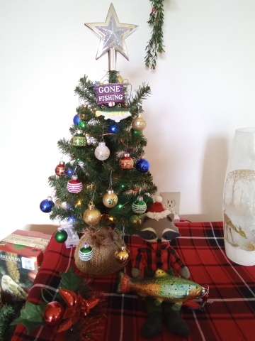 small decorated Christmas tree with stuffed raccoon and glass rainbow trout ornament at its base